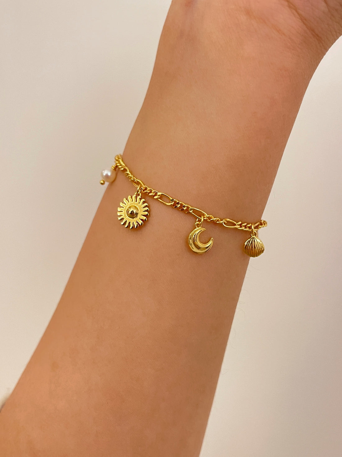 Ocean Heart Armbåndet fra Pallantis Smykker er et guldarmbånd med en justerbar kæde med vedhæng af rose, blad, søstjerne, muslingeskal, halvmåne, sol og to ferskvandsperler på en hvid baggrund.