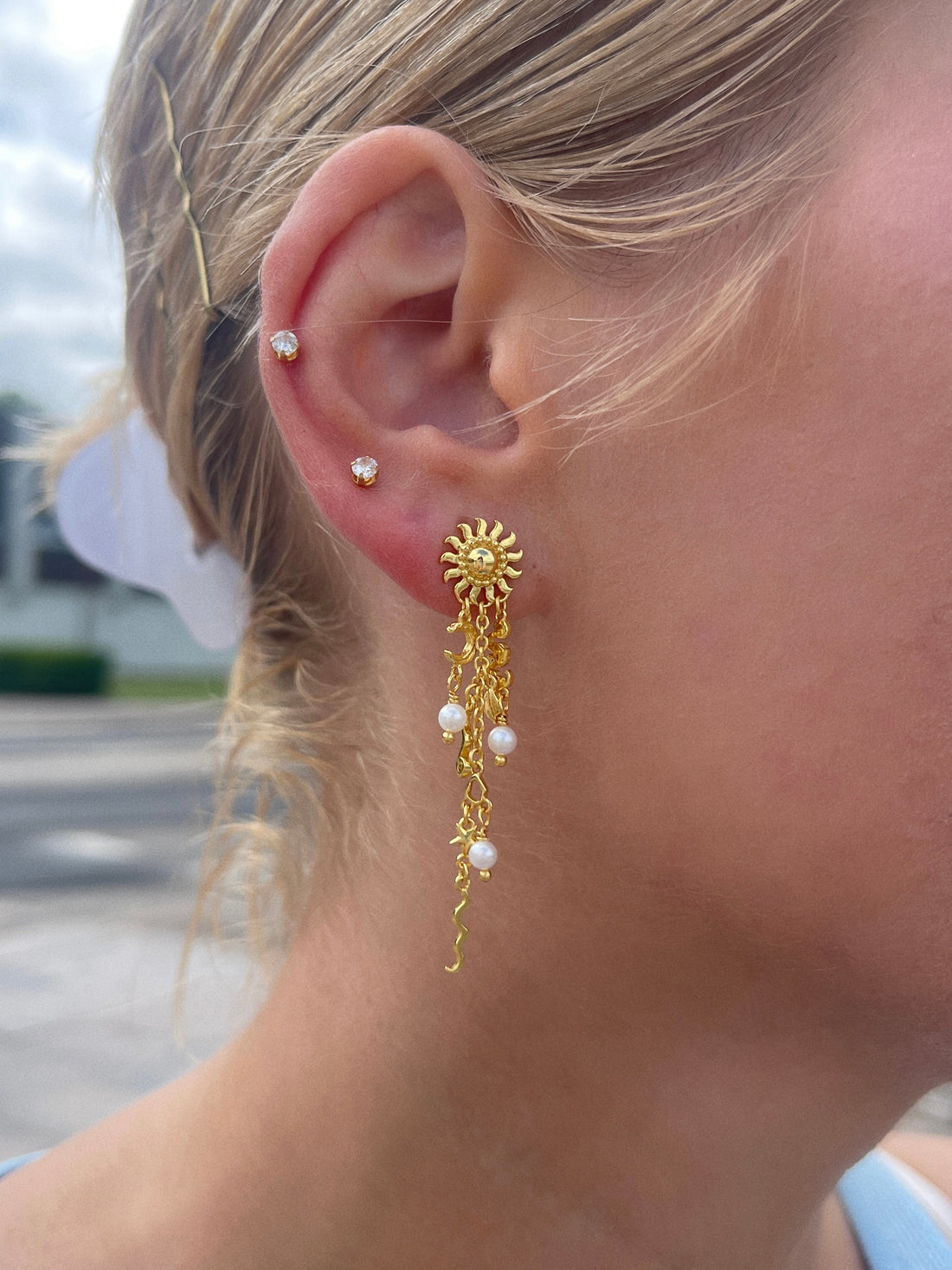 Pallantis Sol Drømme Øreringe fremviser sol-, halvmåne- og stjernemotiver med abstrakte former og ferskvandsperler, alle fremstillet i forgyldt sølv med kæder og bølgede detaljer, der giver et himmelsk look.