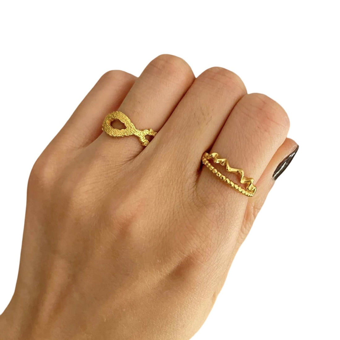 En hånd med sort neglelak på lillefingeren bærer to guldringe: en fiskeformet statement-ring på pegefingeren og Pallantis Måne Krusnings-ringen på langfingeren, alle sat mod en hvid baggrund.