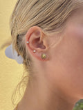 Nærbillede af et øre med to små ørestikker af 925 sterlingsølv på det øvre øre og en Pallantis Smykker Vivian Sol Ørestikker, formet som en gylden sol, på øreflippen. Blondt hår er sat tilbage mod en gul baggrund.