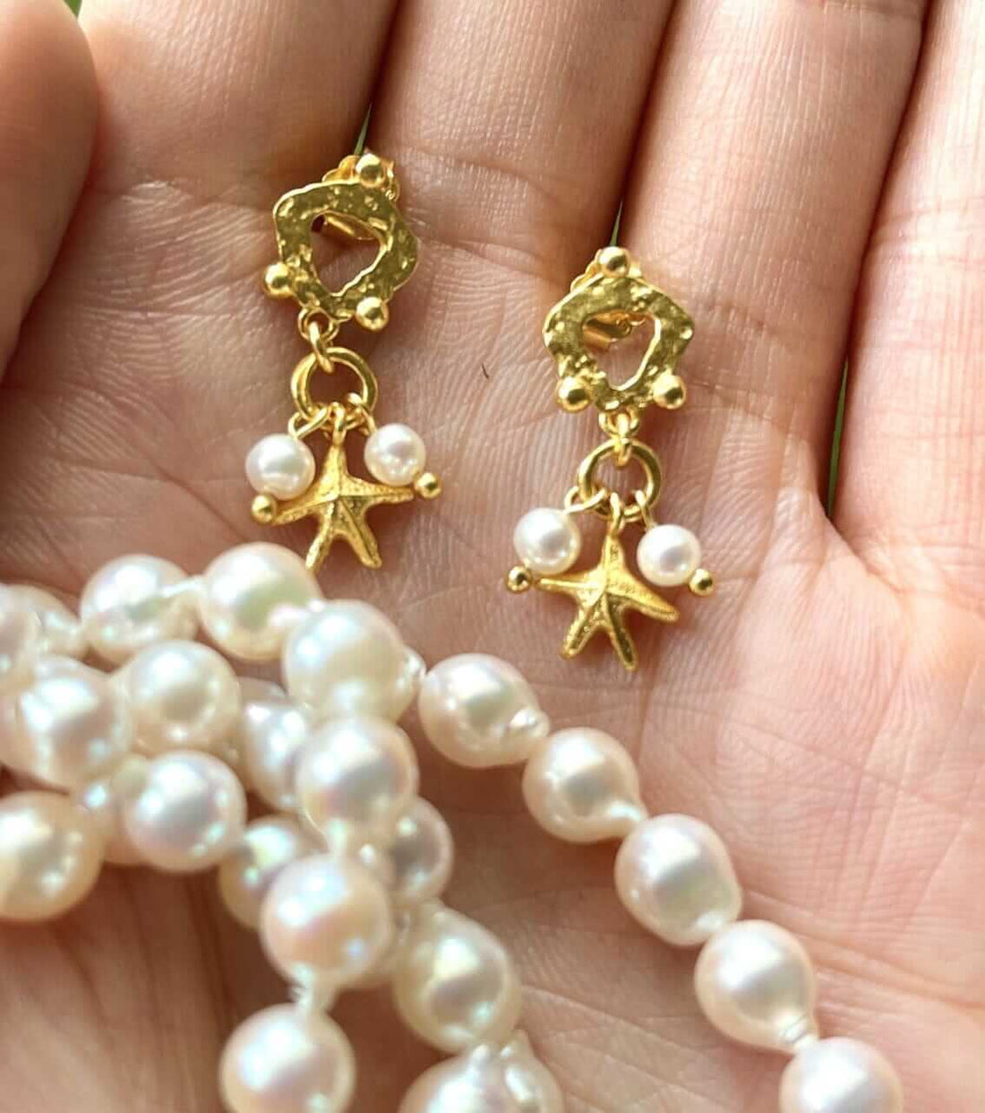 Søstjerner Øreringe fra Pallantis: Forgyldte sølvøreringe med ujævne loops, pyntet med hængende søstjerne og to små ferskvandsperler, vist mod hvid baggrund.